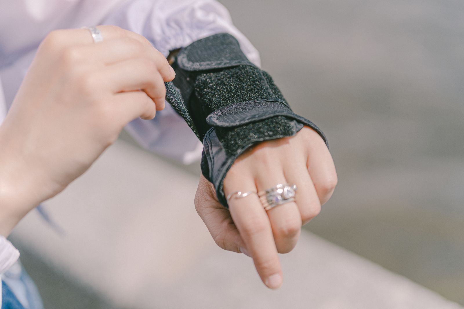 Detailed shot of a hand with rings adjusting a wrist brace, showcasing protection and style outdoors.